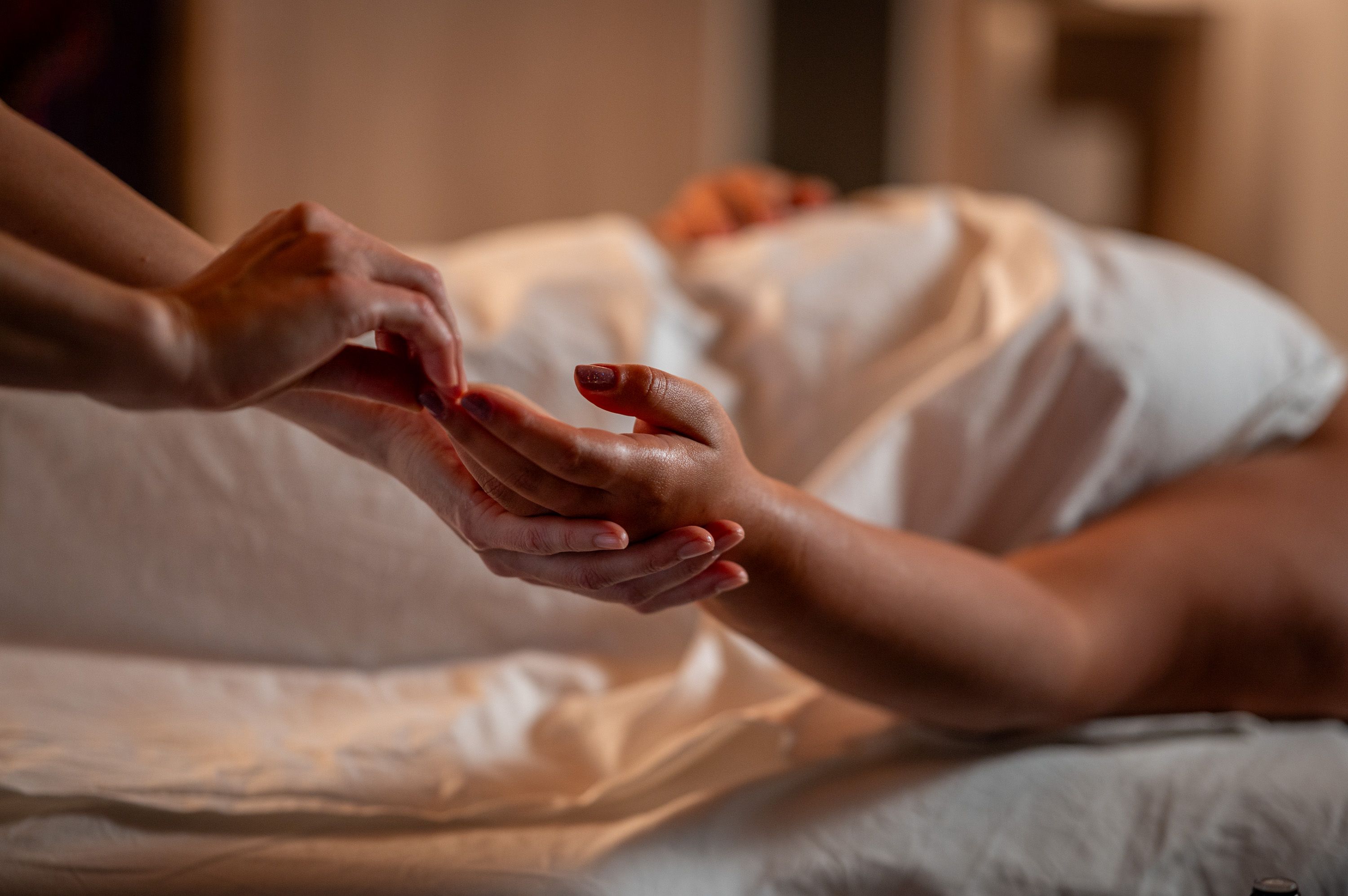 Hände massieren sanft die Hände einer liegenden Person auf einem Bett.